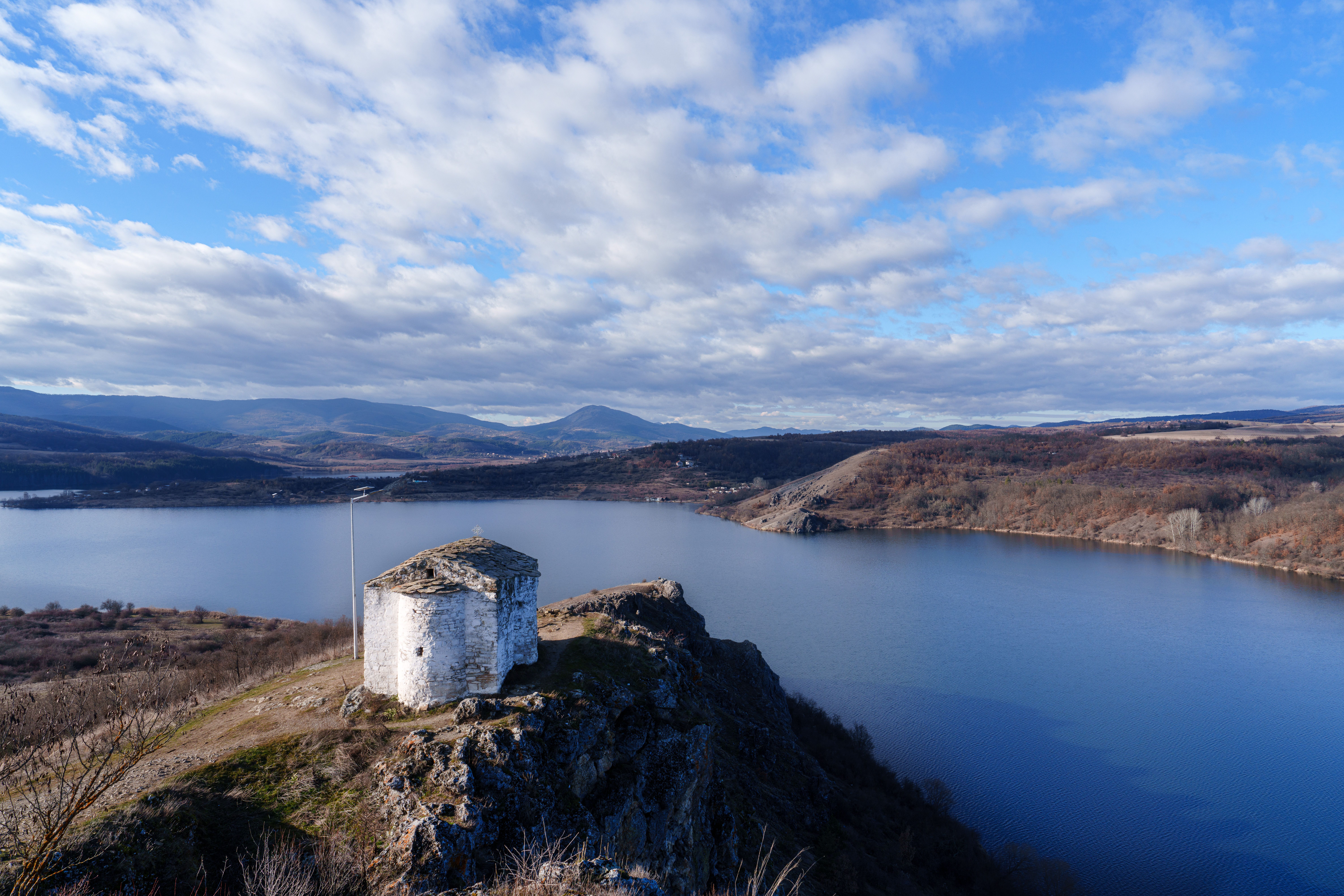 A stunning aerial capture of Pchelina Lake and a historic chapel atop a cliff in Bulgaria.