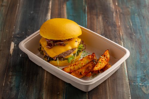 Free Delicious gourmet cheeseburger with wedges in eco-friendly box on rustic table. Stock Photo