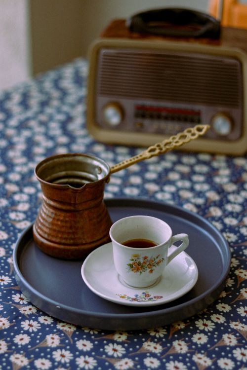 Free A Turkish coffee cup and copper pot on a floral tablecloth, with a retro radio in the background. Stock Photo
