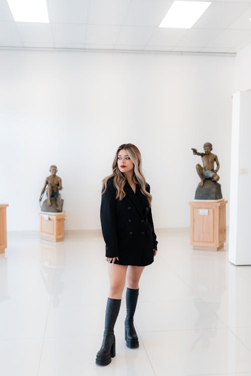 A woman in black boots and a black coat standing in a museum