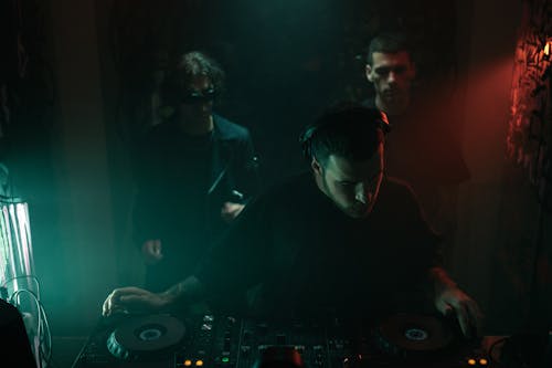Two Men Standing behind the DJ in a Club 