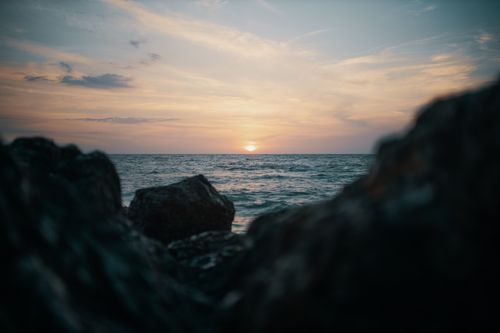 Free A tranquil ocean sunset view with rocky foreground, perfect for nature themes. Stock Photo