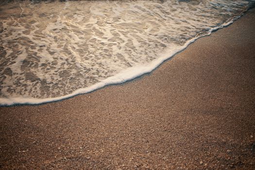 Calm beach scene with waves gently washing ashore over sandy beach.