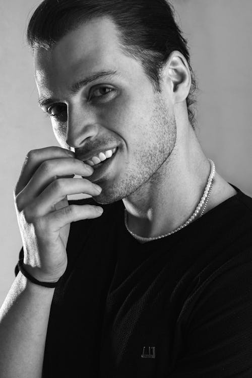 A man in black shirt smiling while holding his hand to his chin