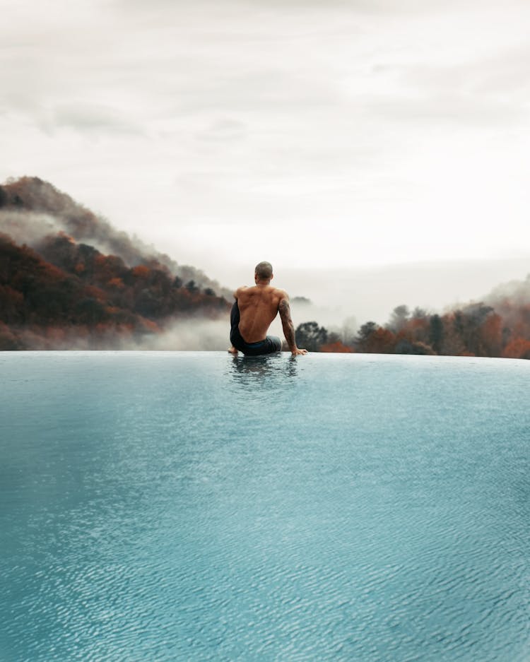 Man Sitting At Pool Over Forest And With Cloud Behind