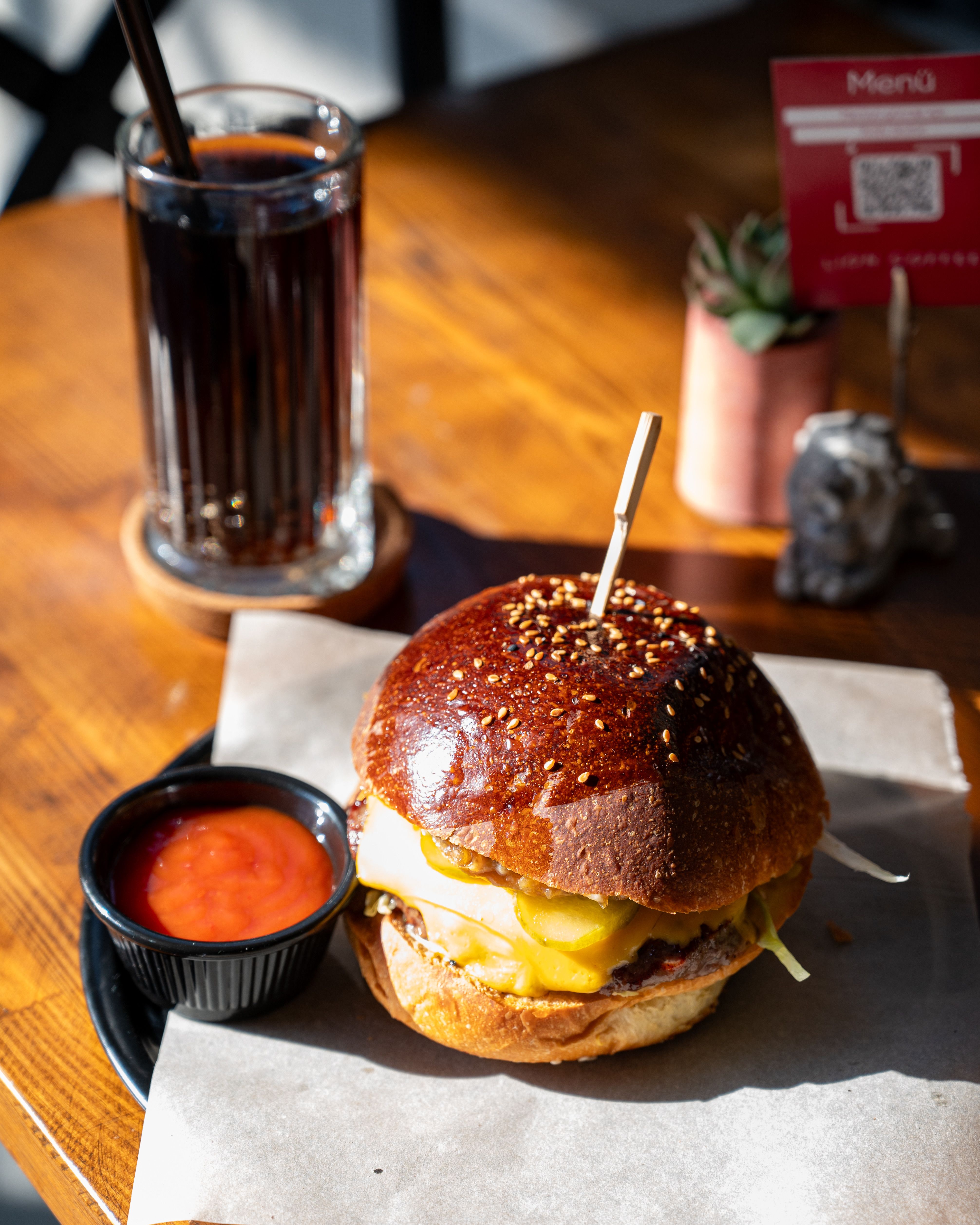 Delicious burger with cheese, served with a cola drink in a sunny dining setting.