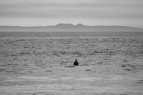 Free Black and white silhouette of a person standing in the ocean with a distant island horizon. Stock Photo