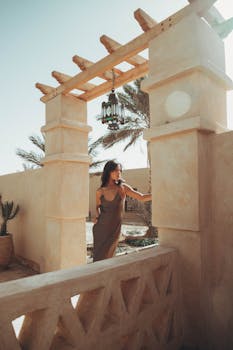 A stylish woman in a spaghetti strap dress stands gracefully under a Moroccan arch.