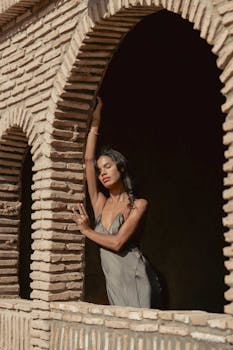 A woman in a stylish gray dress poses gracefully by arched windows in Marrakesh.