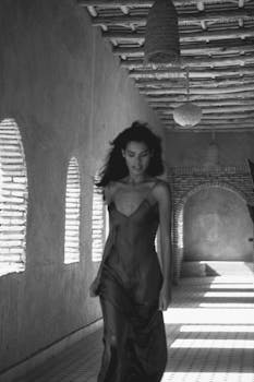 Black and white image of a woman in a dress walking through an arched hallway in Marrakesh, Morocco.