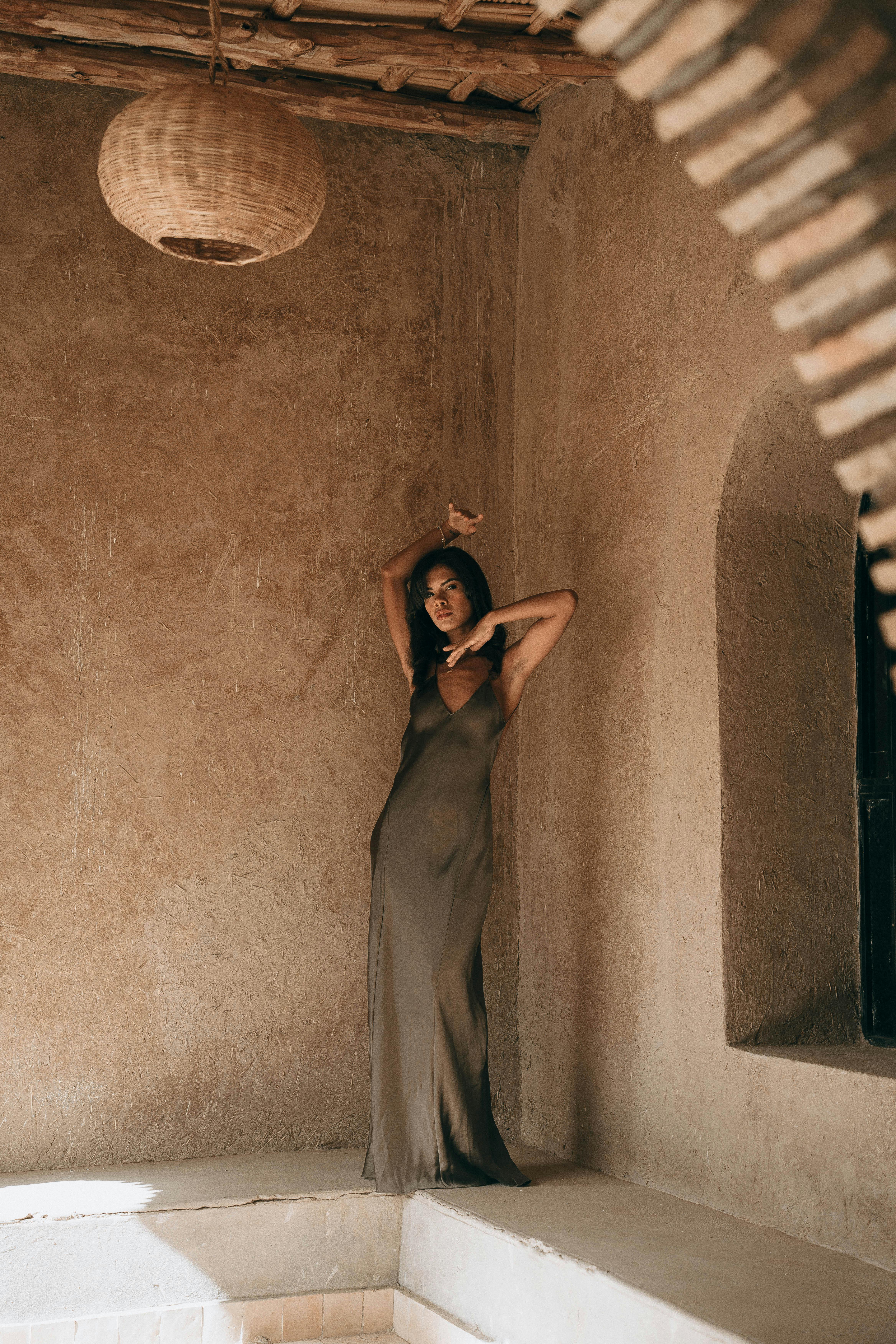 A stylish woman poses gracefully in a spaghetti strap dress in a rustic Marrakesh setting.