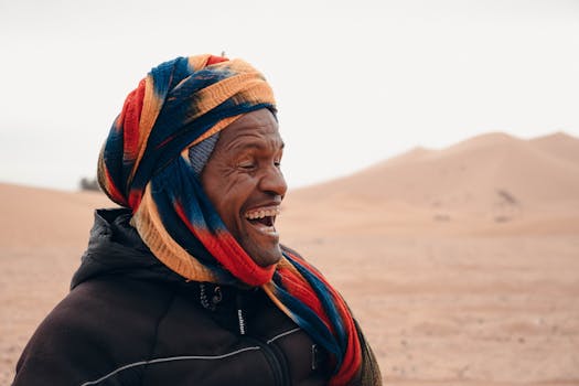 Joyful Bedouin man laughing in the desert, wearing a vibrant headscarf.