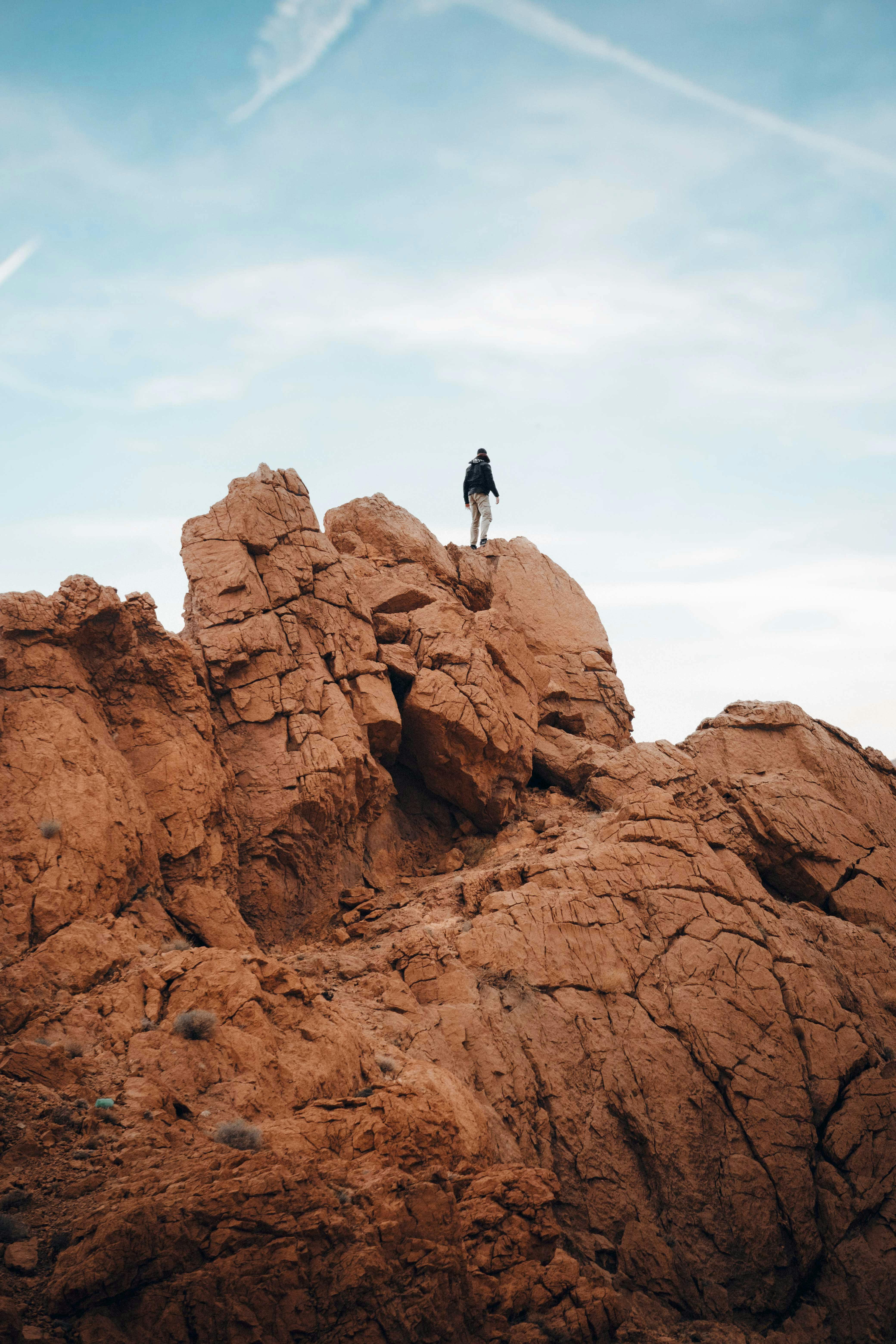 A solitary figure stands atop a rugged cliff under a sunny sky, embracing adventure.