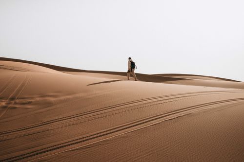 Free A lone man hiking across vast desert sand dunes with a backpack, showcasing adventure. Stock Photo