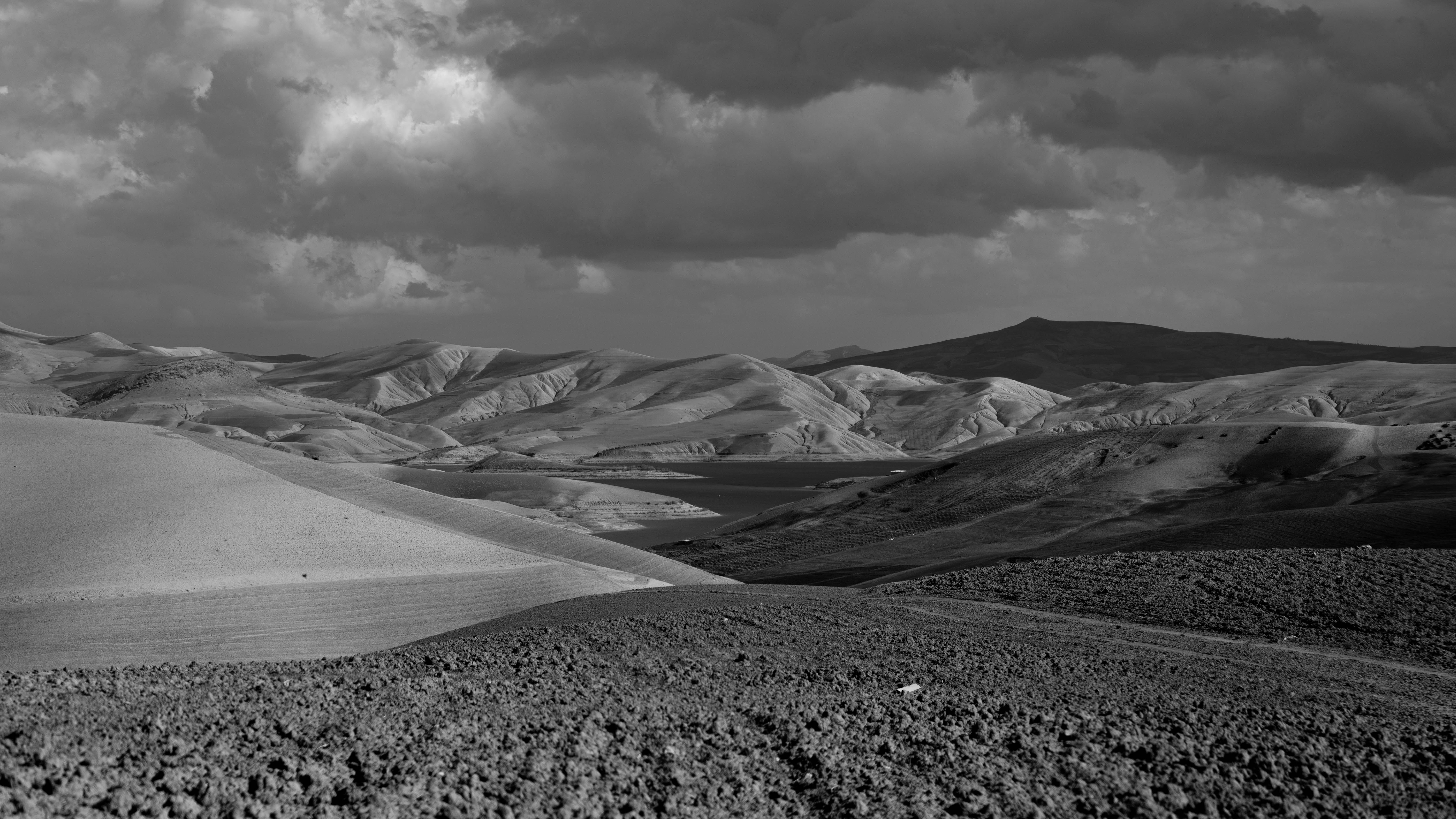 Panoramic black and white view of an arid mountain landscape under dramatic skies.
