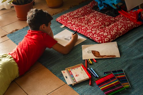 A child laying on the floor with a pencil and coloring book