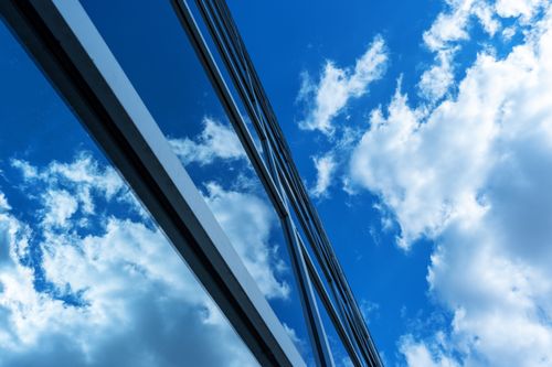 Free A sleek modern building with reflective glass windows and a clear blue sky with clouds. Stock Photo