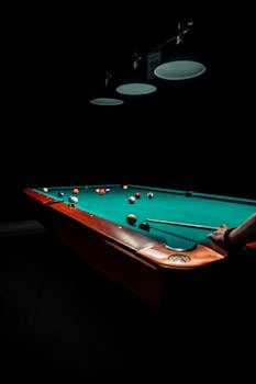 A dramatic and focused image of a billiards game under dim lighting, highlighting the intensity of the sport.