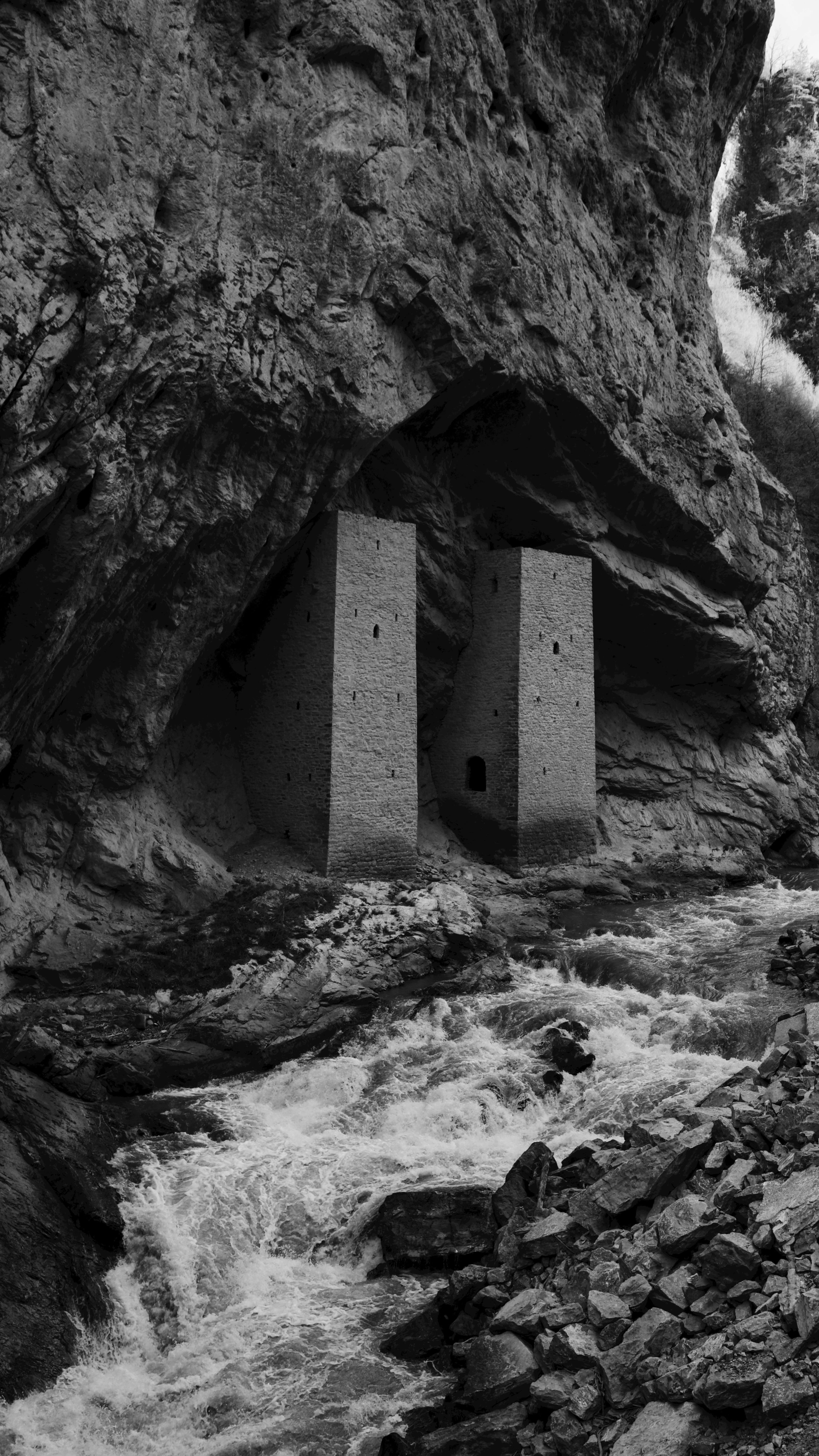 Dramatic black and white shot of ancient fortress amidst rugged rocks and flowing river.