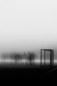 Ethereal black and white image of soccer goal and figures in foggy motion on the field.