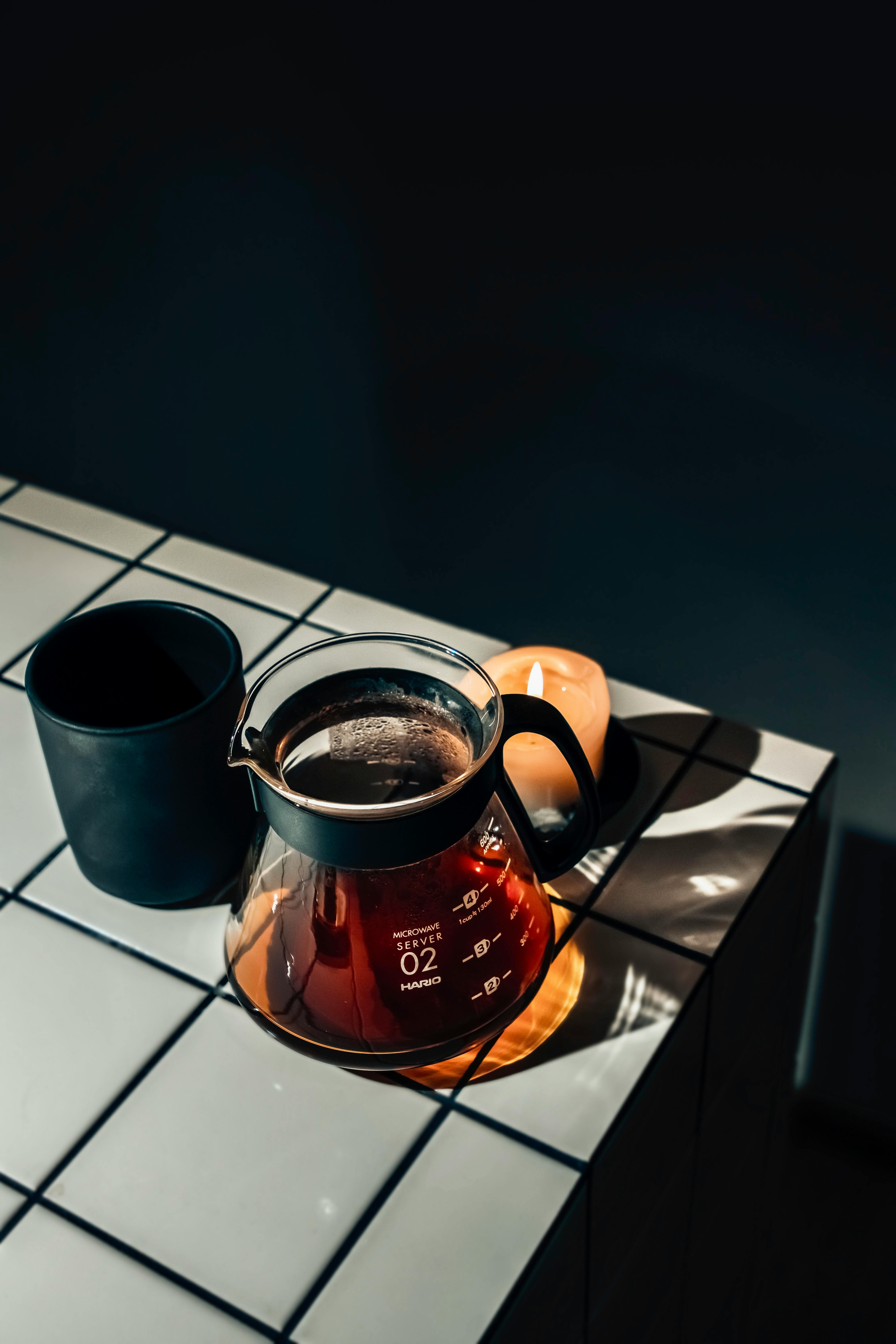 Stylish still life with a teapot, mug, and candle on a modern tiled counter under dramatic lighting.