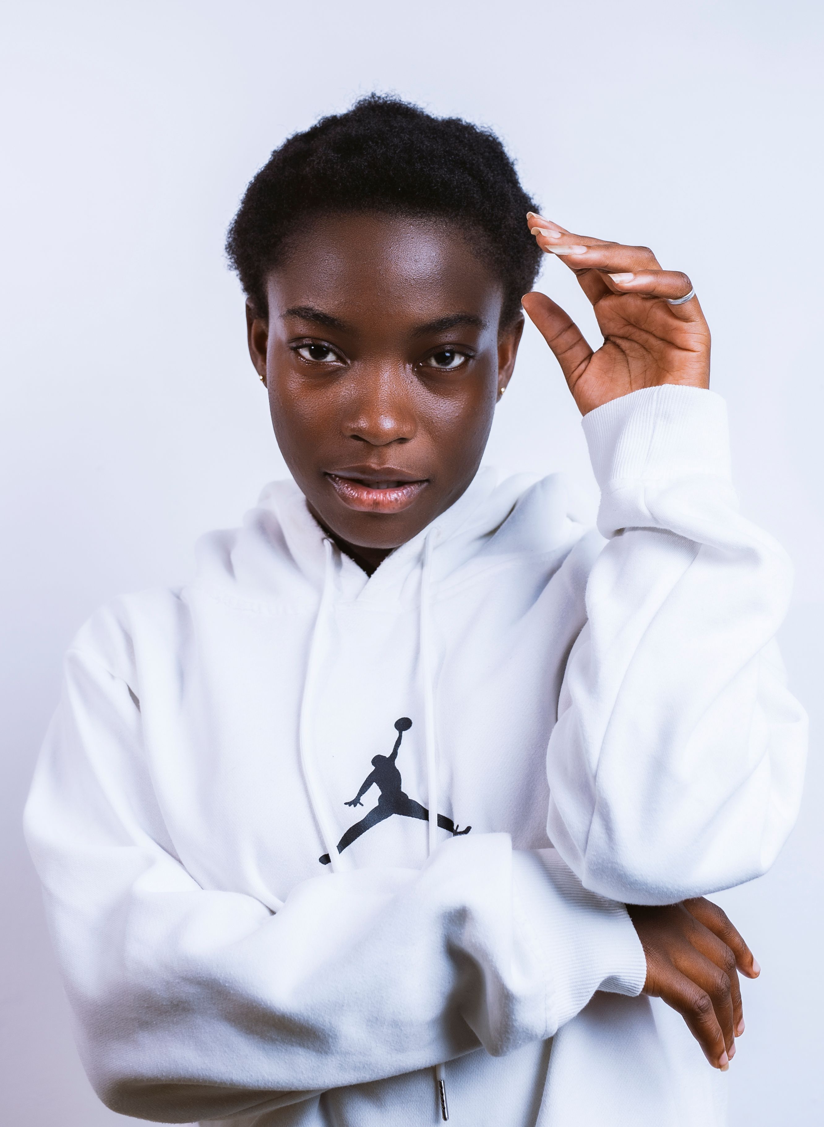 Portrait of a stylish teenager in a white hoodie, posing confidently against a white background.