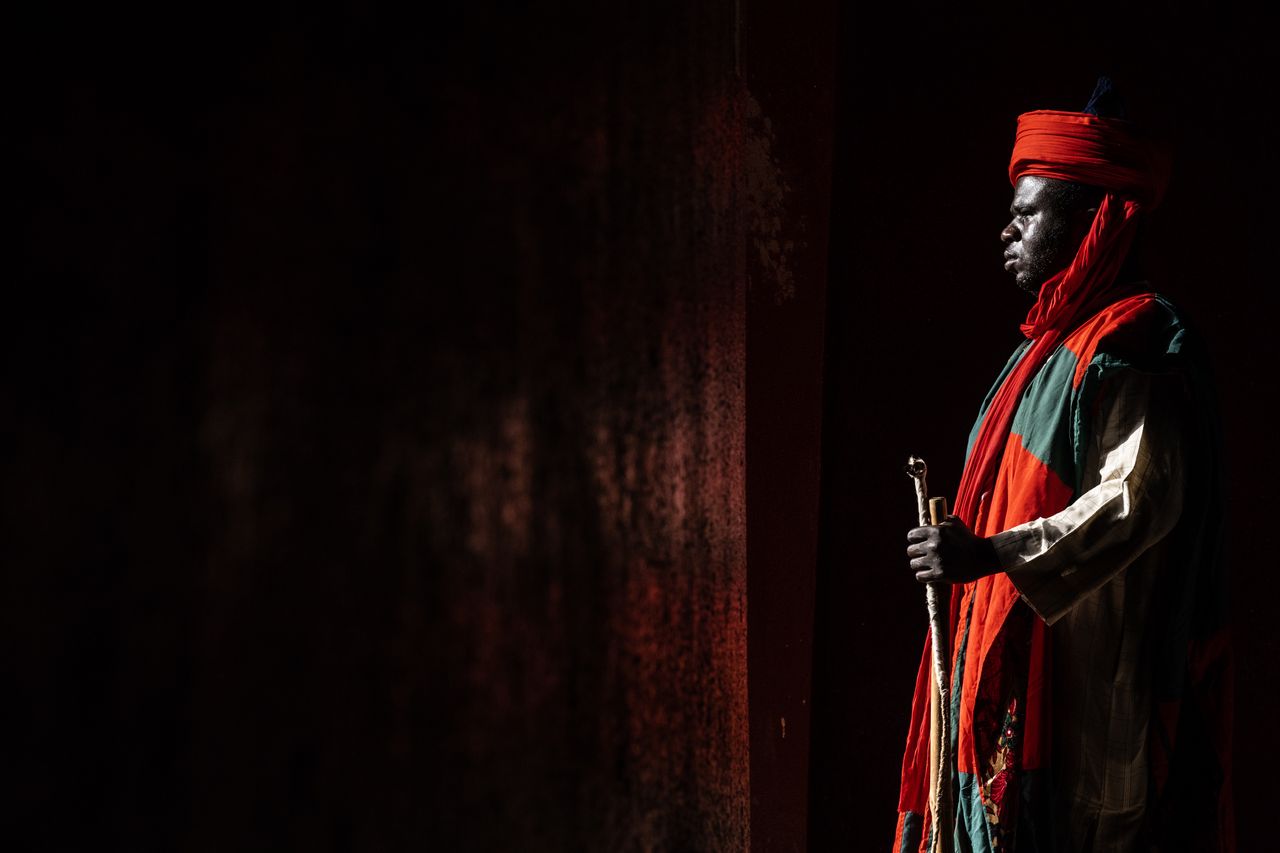 a man in traditional attire with vibrant colors standing in shadows ho