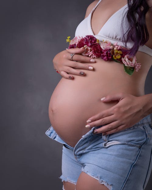 A pregnant woman in denim shorts and a flower in her belly