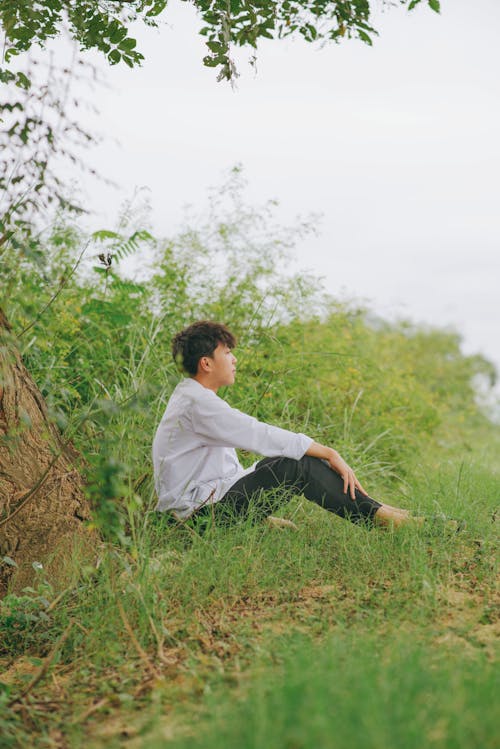 A young man sitting on the ground near a tree