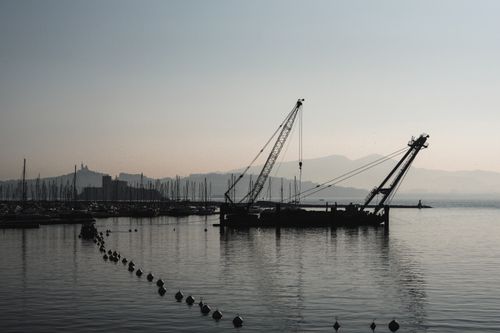 Free A serene view of a dredger silhouetted against a misty harbor at dawn. Stock Photo