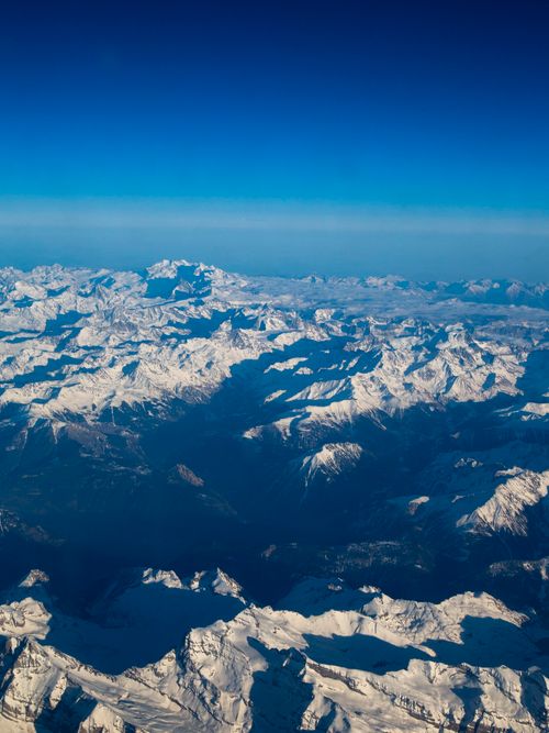 Free Stunning aerial view of a vast snow-covered mountain range under a clear blue sky. Stock Photo