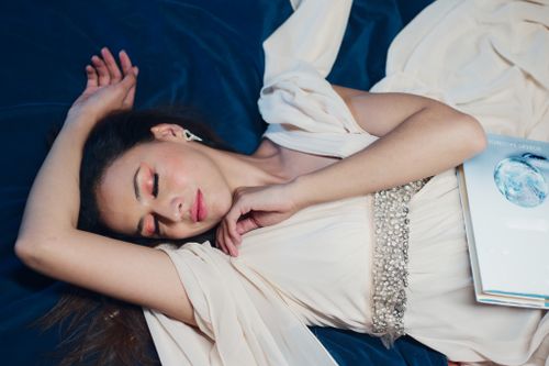 Free A serene woman lies gracefully on a bed in a flowing dress, exuding elegance and tranquility. Stock Photo