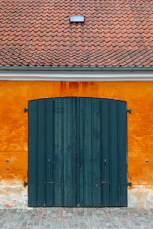 Free Close-up of a wooden gate on an orange wall with a tiled roof, showcasing rustic architecture. Stock Photo