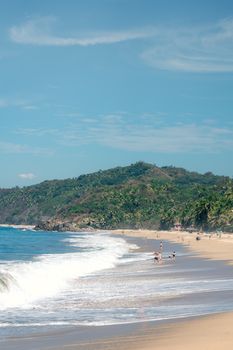Relaxing tropical beach scene with waves, hills, and people enjoying the ocean view.