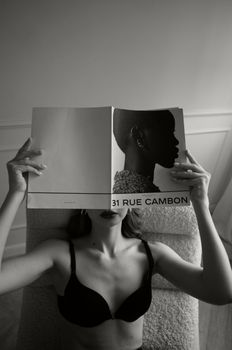 Stylish portrait of a woman sitting indoors, reading a fashion magazine.