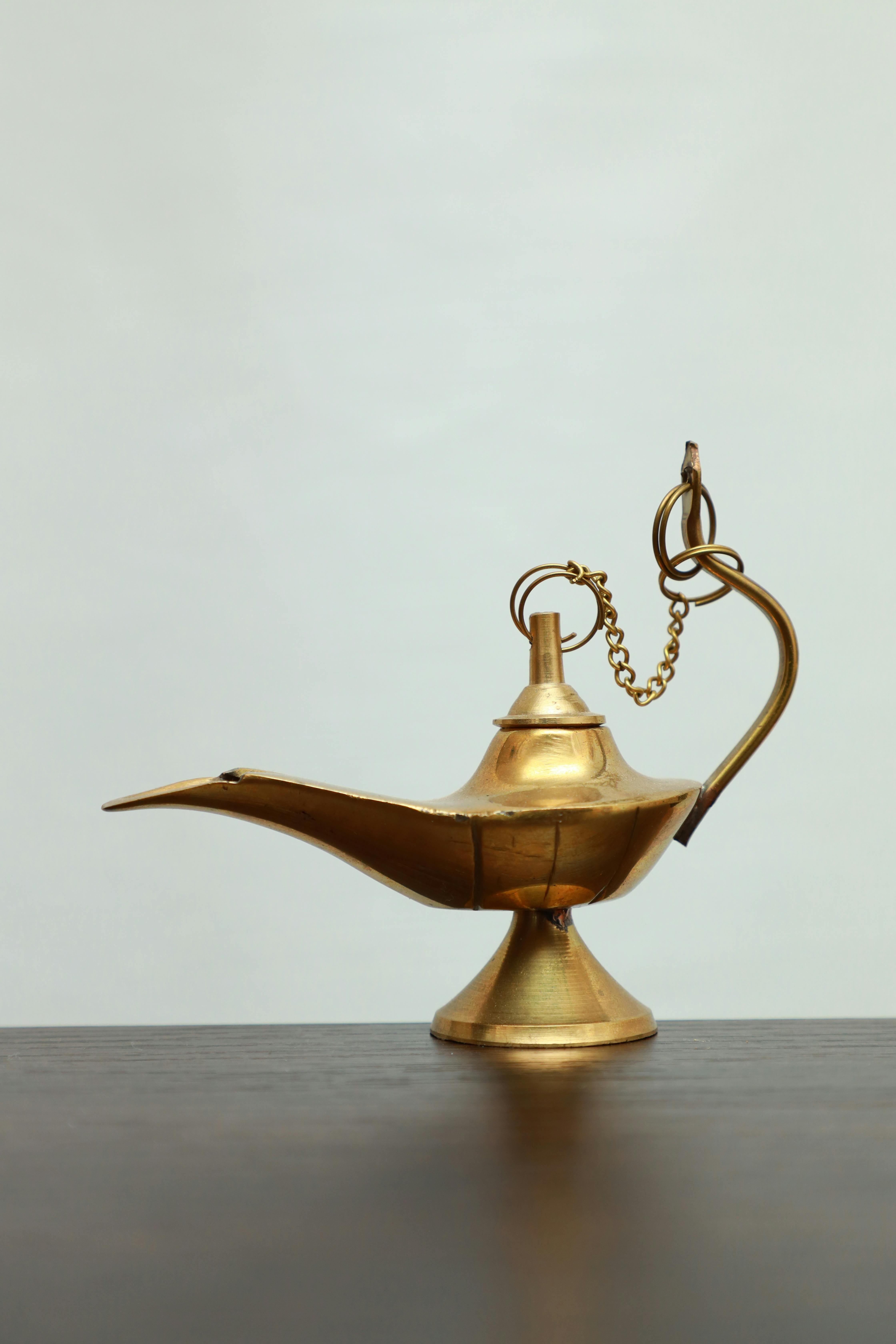 Close-up of an ornate antique brass oil lamp with chain detail, set against a neutral backdrop.