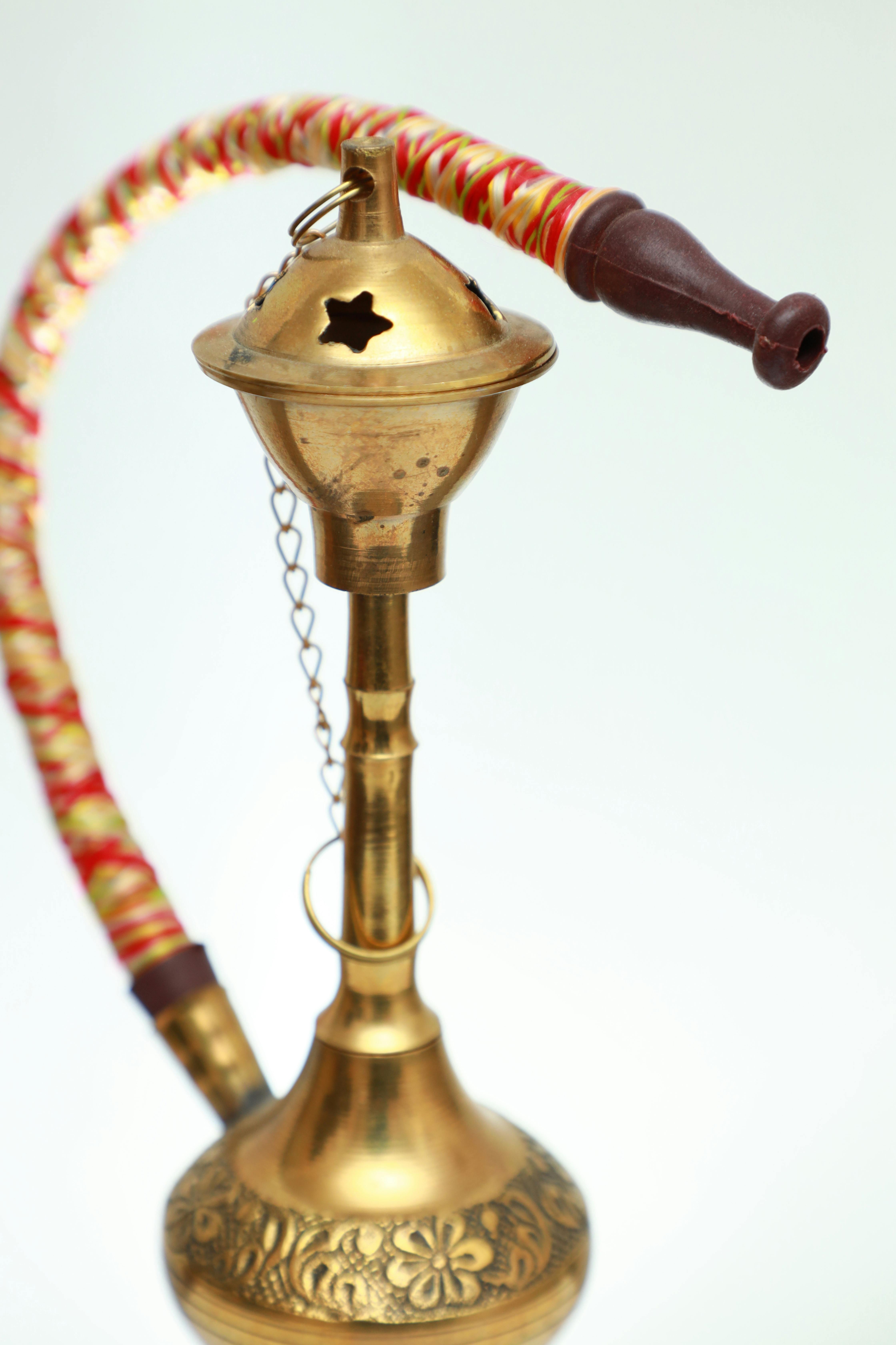 Elegant antique brass hookah with intricate designs and red hose, isolated on a white background.