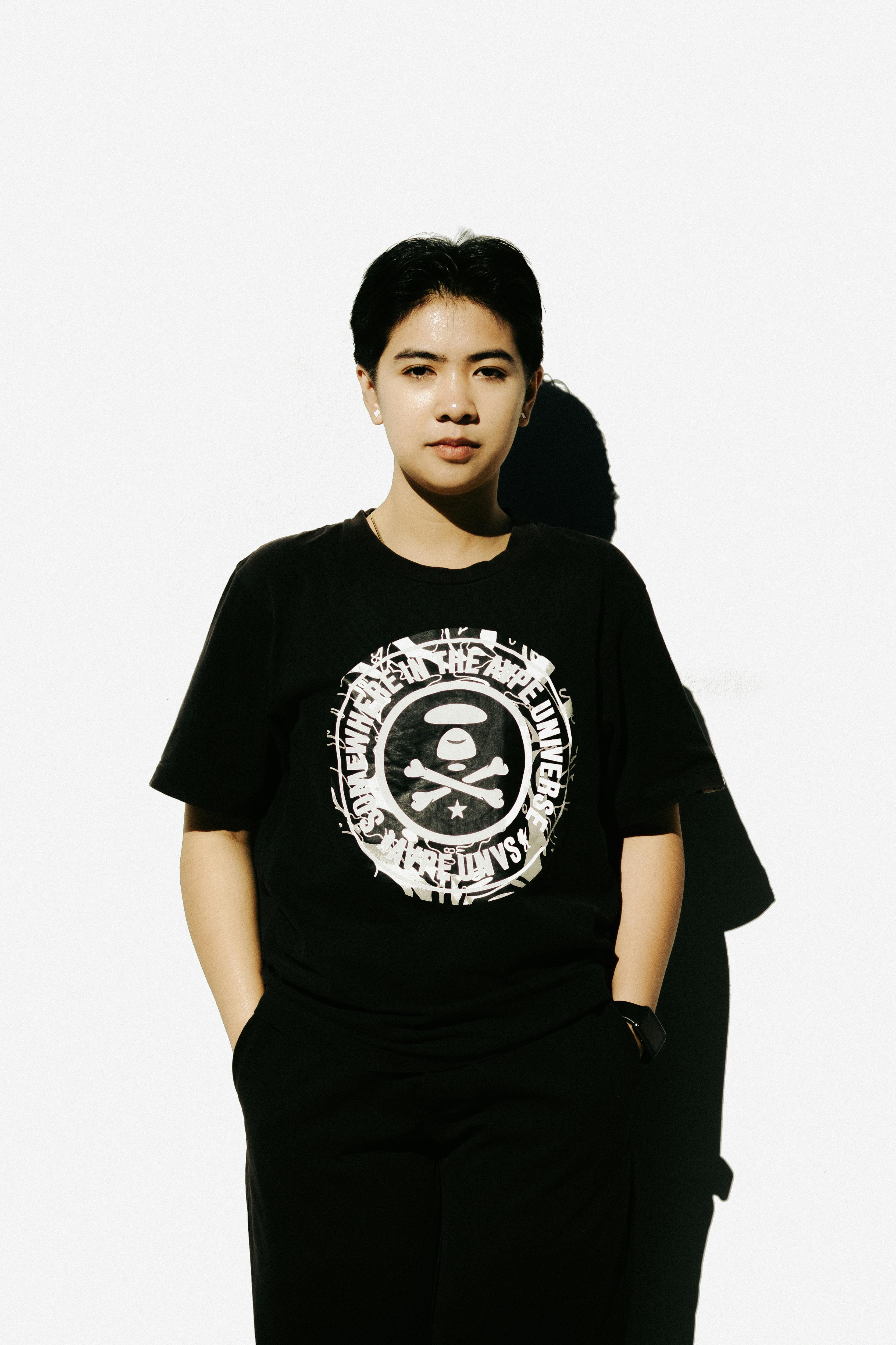 Stylish young woman posing in black printed T-shirt against a minimalist white backdrop.