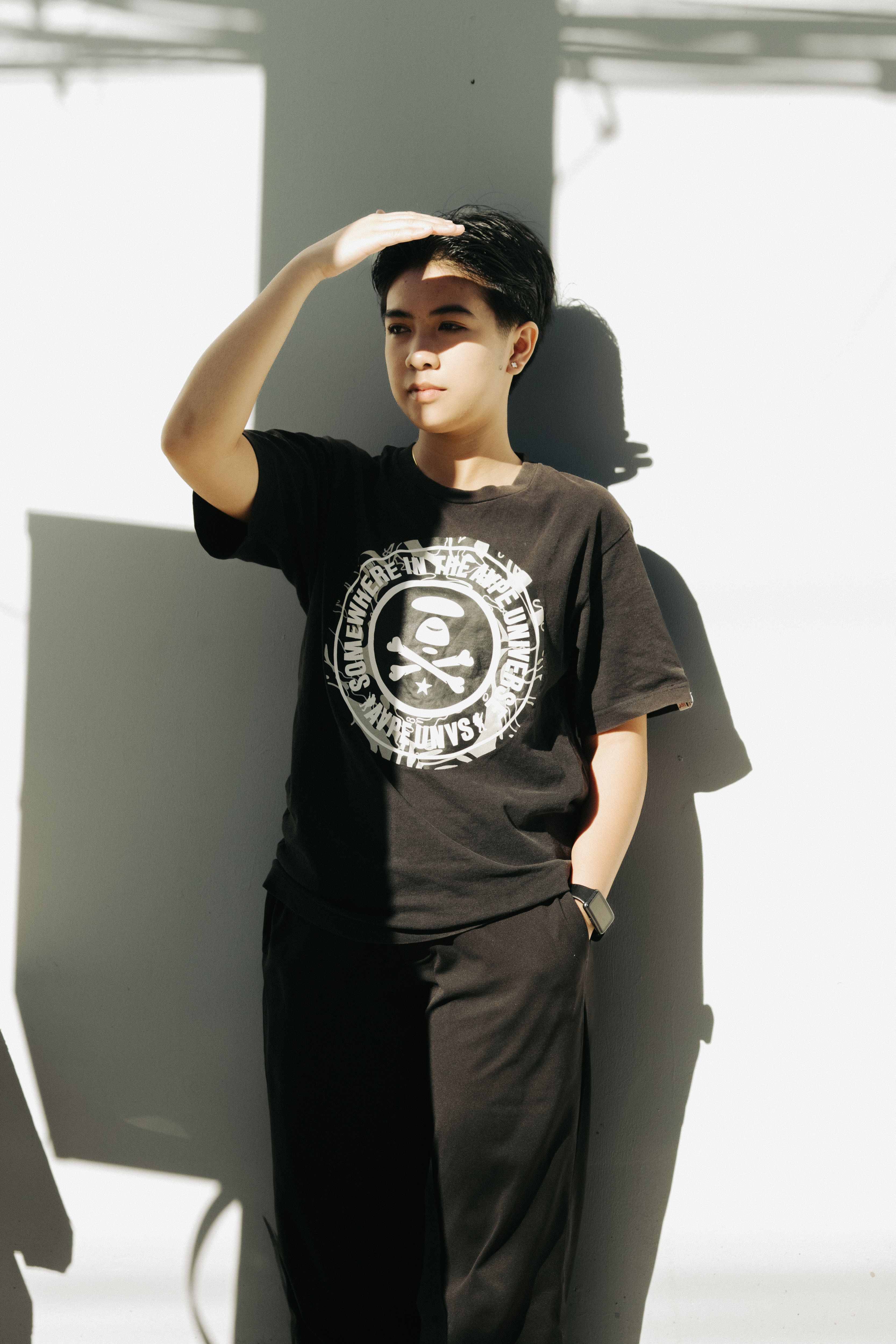 Portrait of a young adult posing outdoors in casual black clothes, casting a distinctive shadow.
