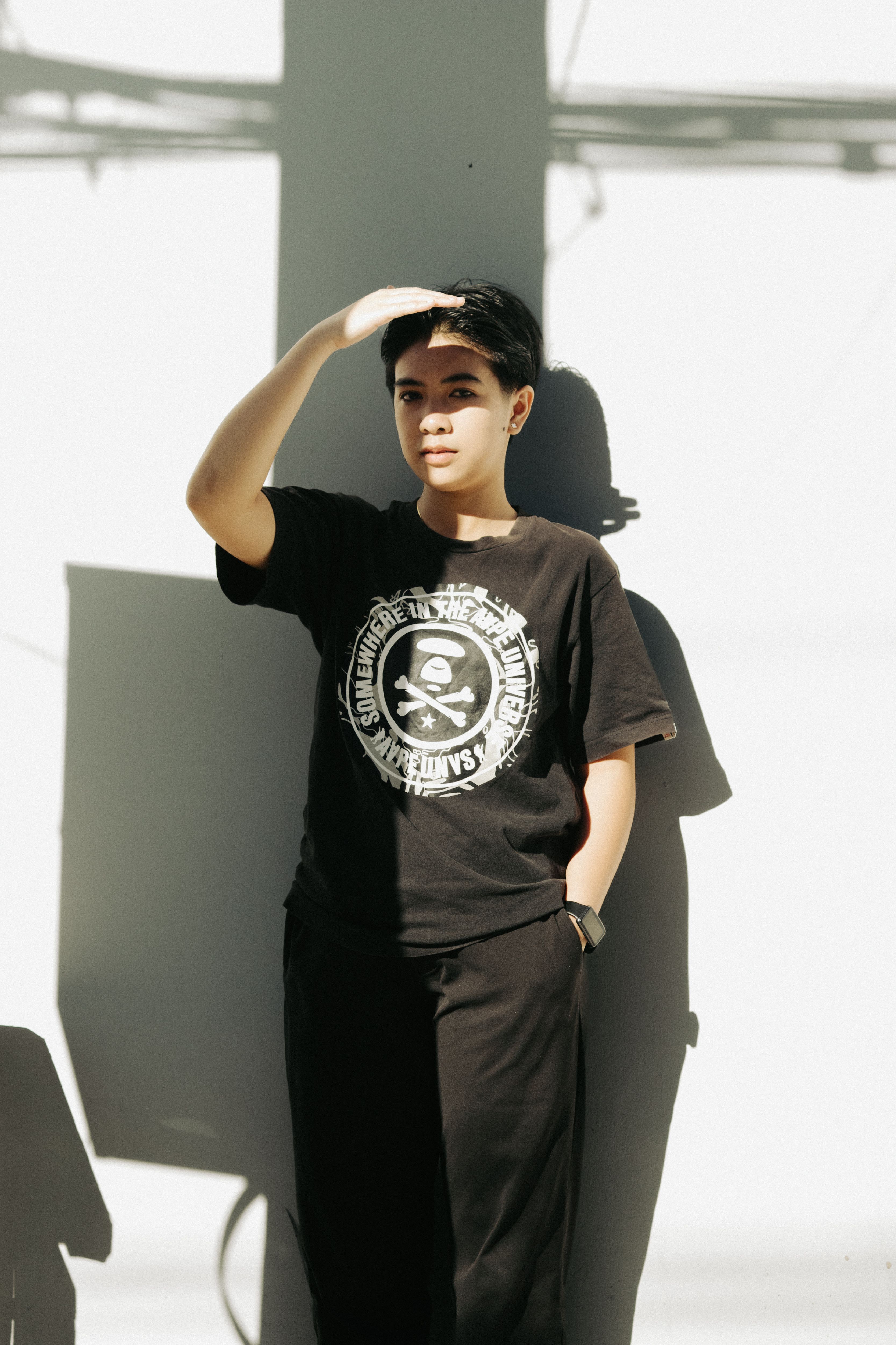 Fashionable young adult in a black t-shirt posing with shadow play indoors, showcasing modern street style.