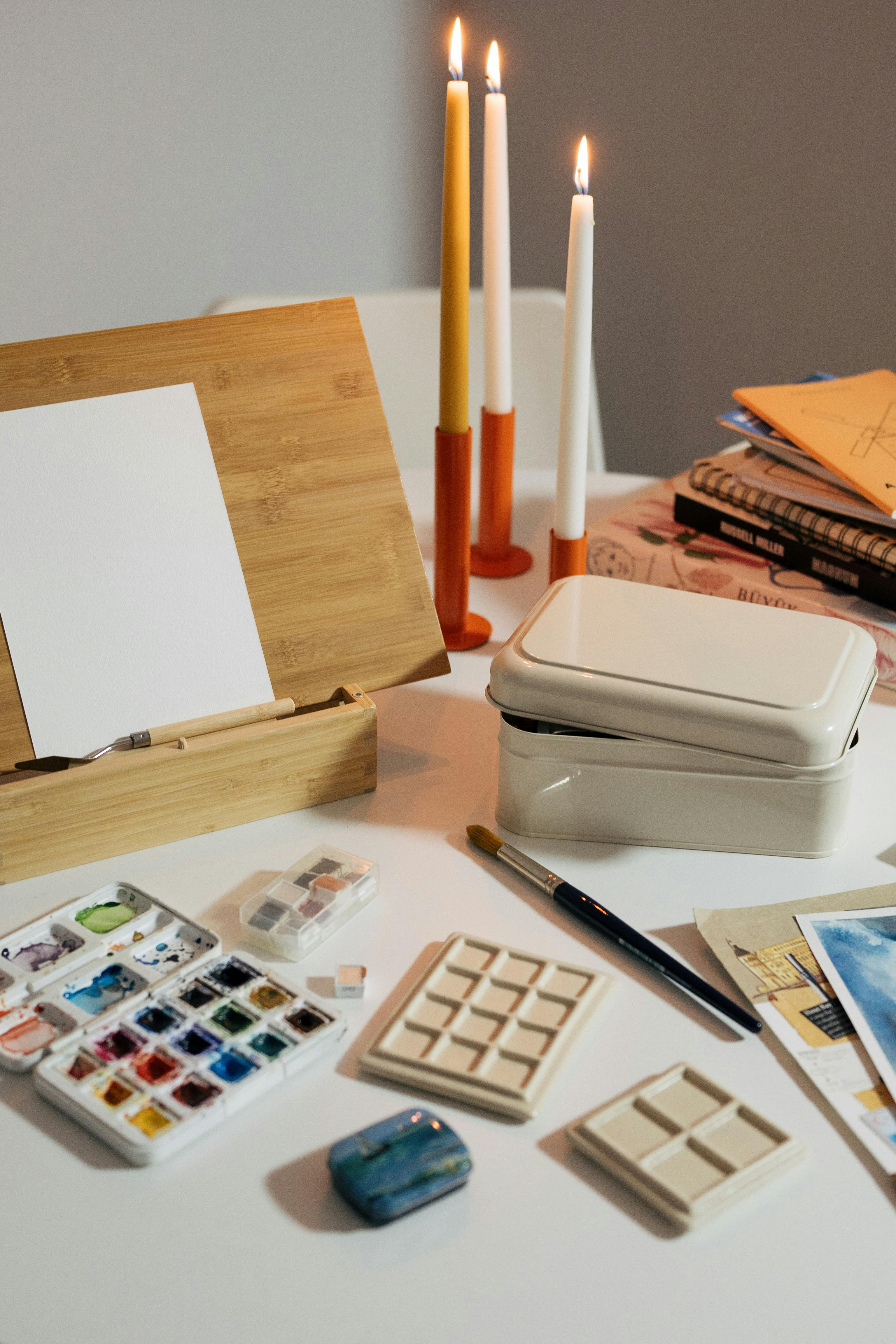 A cozy and organized art setup with watercolor paints, brushes, and candles, perfect for relaxation and creativity.