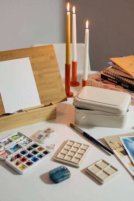 A cozy and organized art setup with watercolor paints, brushes, and candles, perfect for relaxation and creativity.