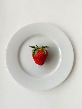 Bright red strawberry displayed on a minimal white plate, top view.