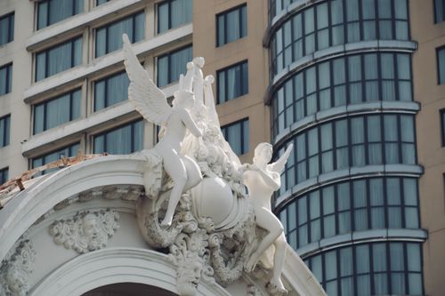 Free Close-up of intricate white sculptures on a classical building facade with modern city backdrop. Stock Photo
