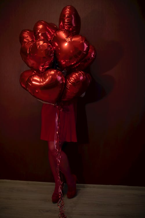 A woman in red stockings holding a bunch of red heart balloons