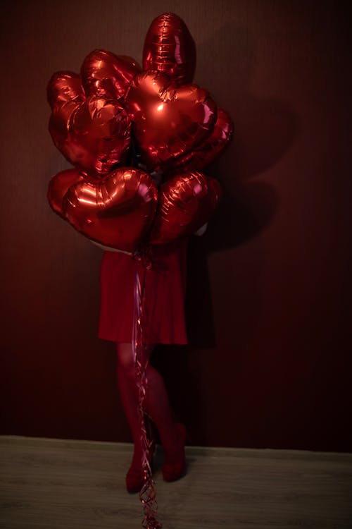 A woman in red stockings holding a bunch of red heart balloons