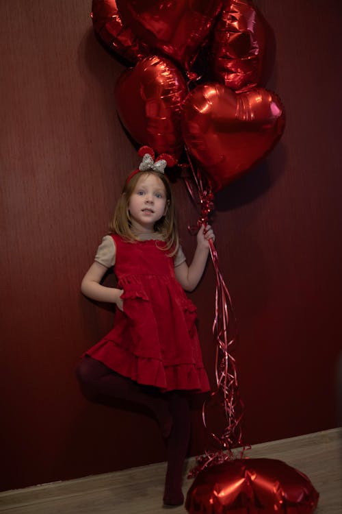 A little girl in red holding a bunch of red balloons