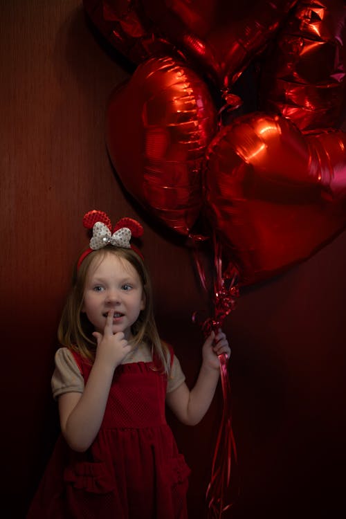 A little girl holding a bunch of red heart balloons