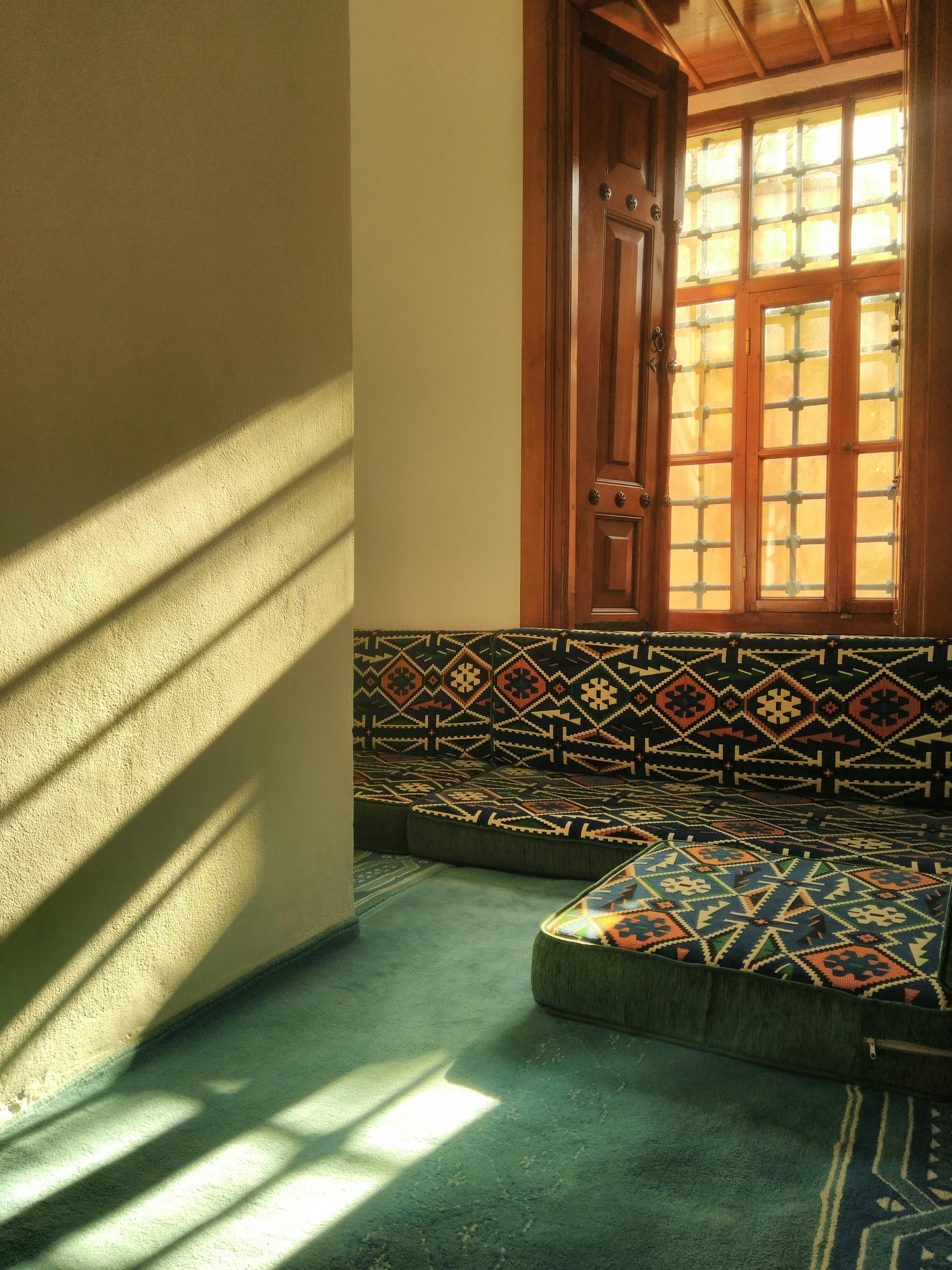 A sunlit room interior featuring traditional patterned carpets and a wooden window.