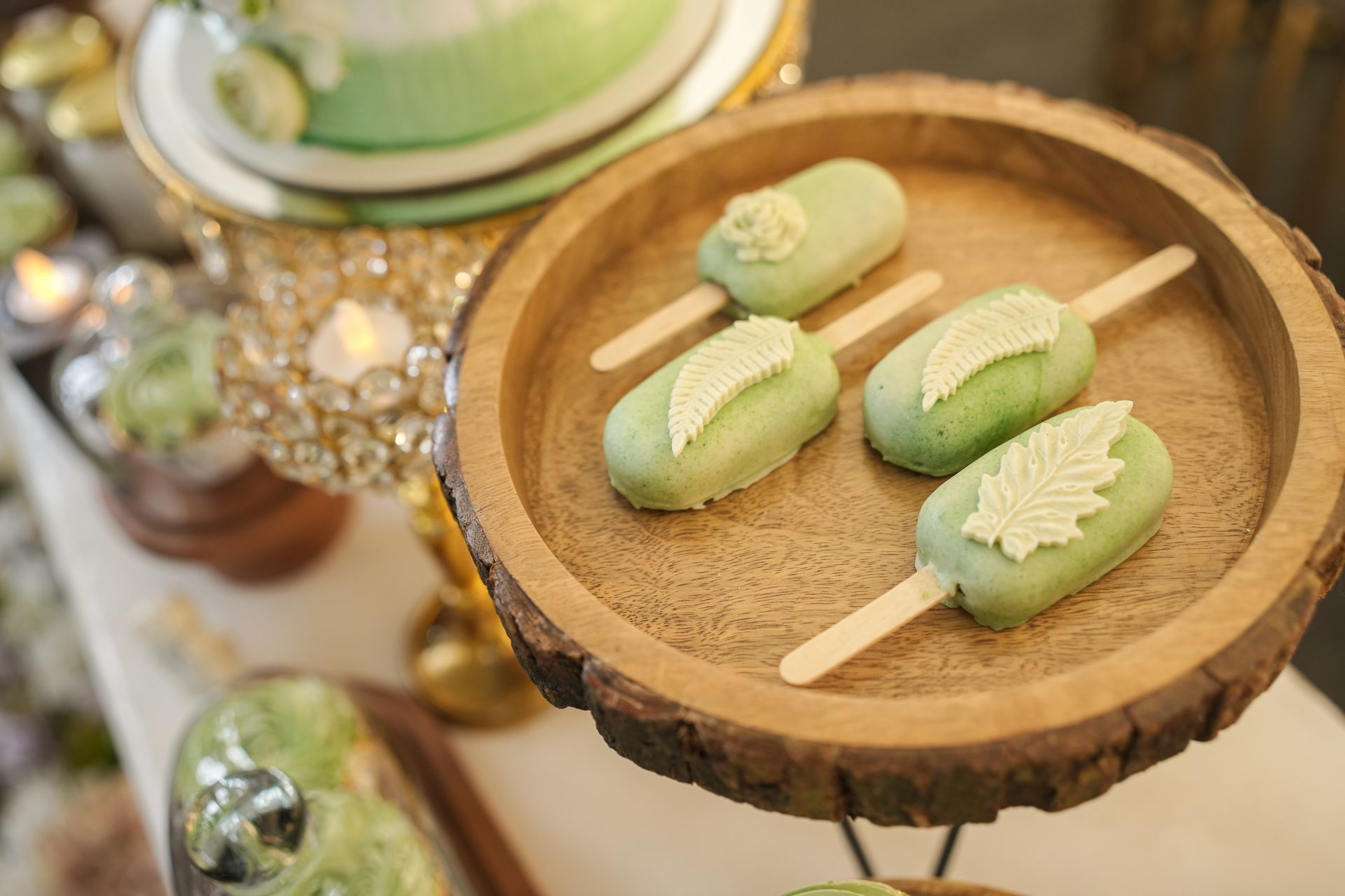 Close-up of green cake pops with leaf designs on a rustic wooden tray at a lavish dessert table.